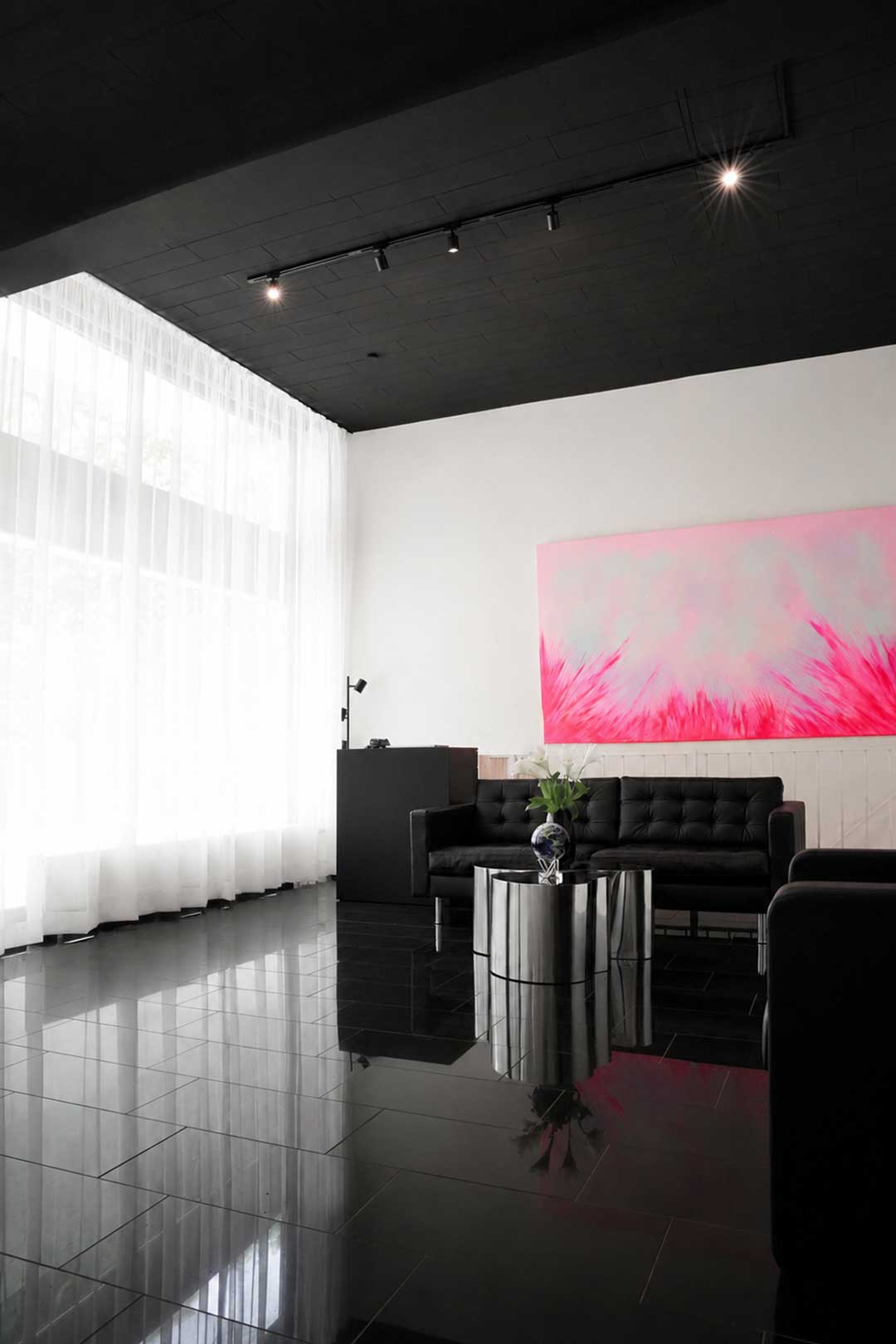 Wartebereich mit schwarzem Sofa und pinkfarbenem Wandbild im Salon